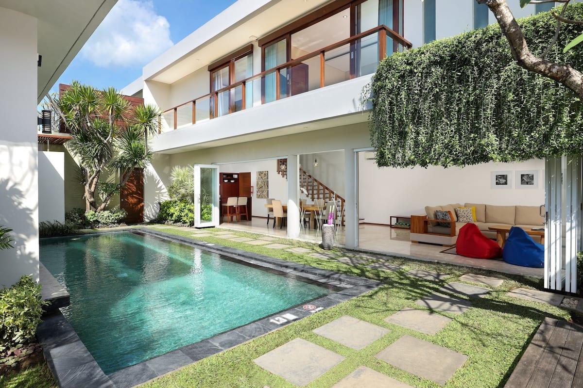 A modern house with a swimming pool, a covered patio, and a staircase leading to a second floor.