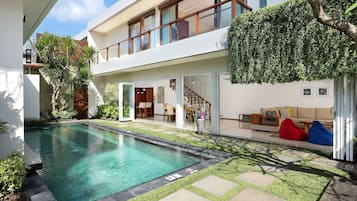 A modern house with a swimming pool, a covered patio, and a staircase leading to a second floor.