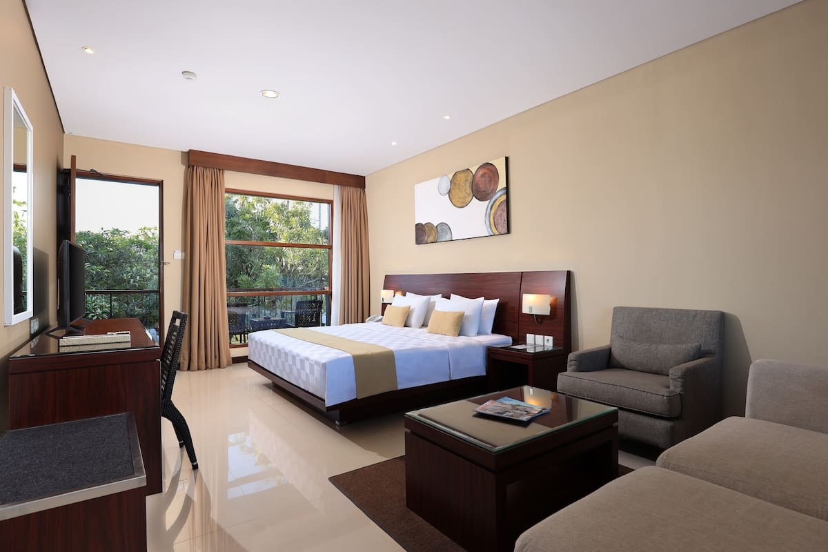 A hotel room with a large bed, a desk, a chair, a sofa, and a window with curtains.