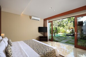Quarto de hotel com uma cama, uma televisão e vista para um jardim através de grandes portas de vidro deslizantes.