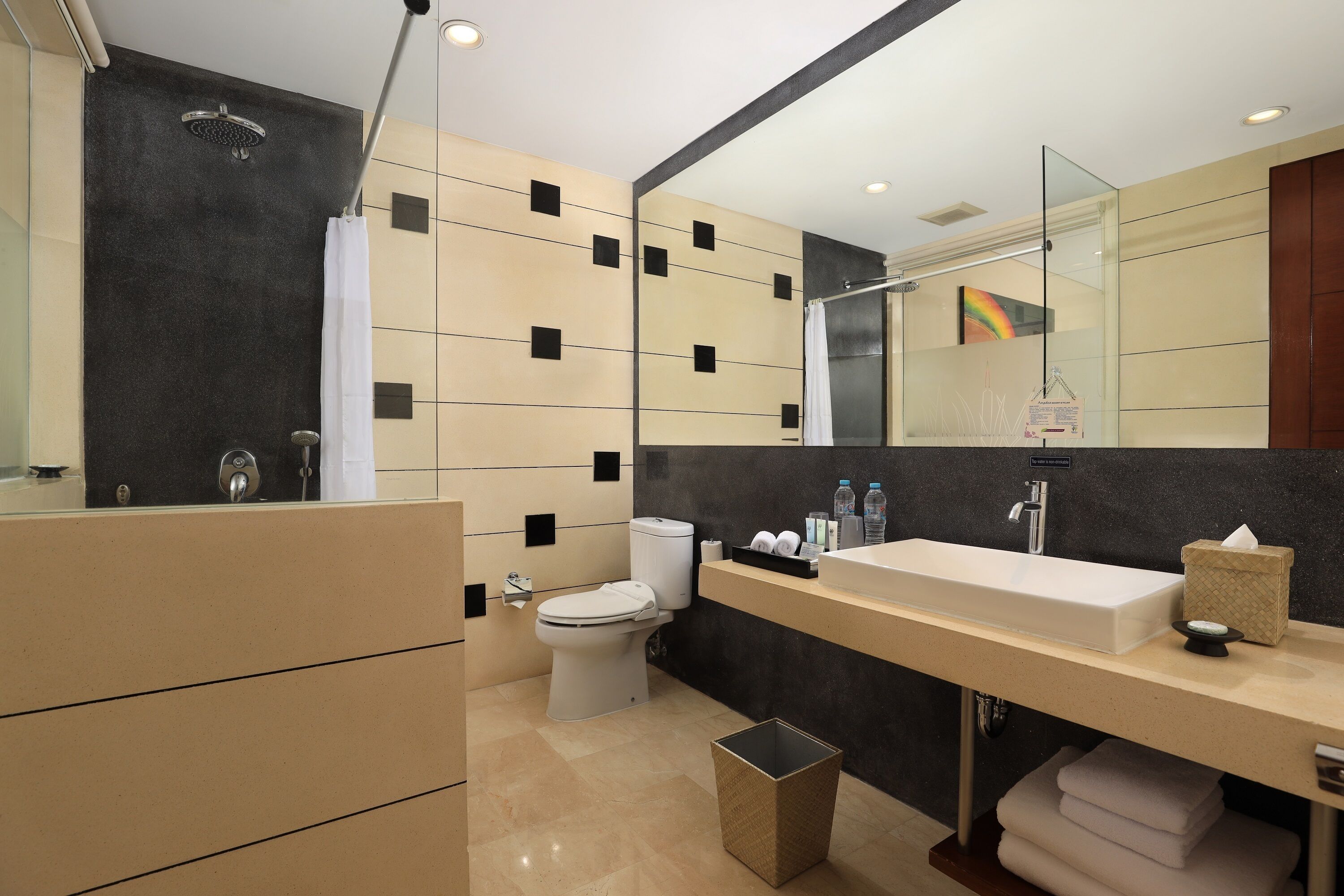 A modern bathroom with a large mirror, a white sink, a toilet, and a shower.