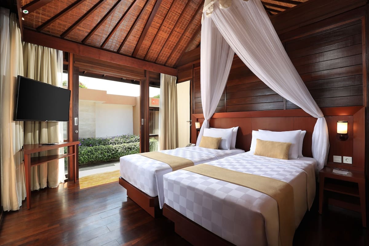 A hotel room with two beds, a TV, wooden flooring, and a canopy bed.