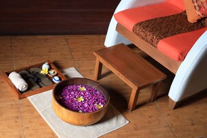 Un vassoio di legno con asciugamani e ciabatte, una ciotola di legno con fiori viola e un piccolo tavolino di legno.