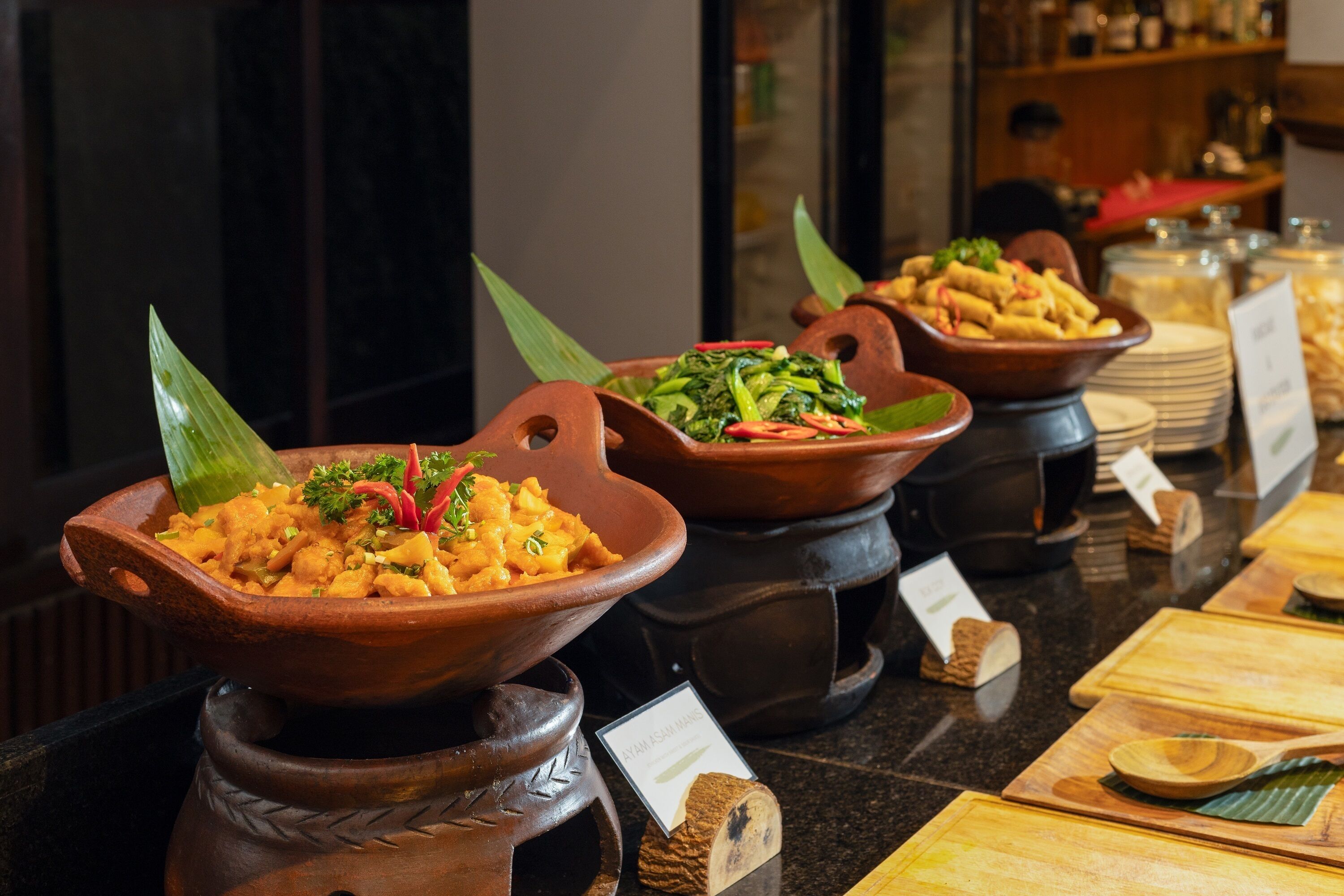 Un bufé con diversos platos servidos en cuencos de barro tradicionales, cada uno con una etiqueta de precio.