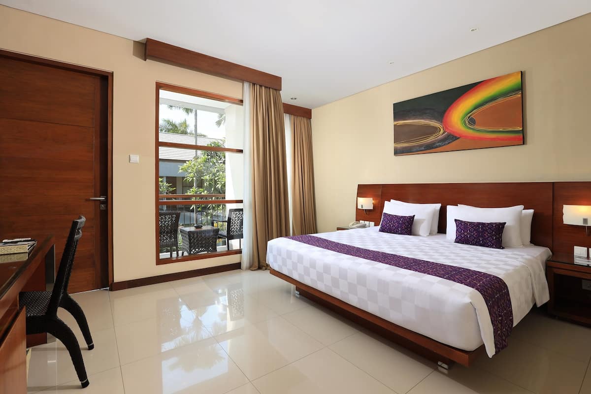 A hotel room with a large bed, a desk, and a chair. There is a window with curtains and a view of the outdoors.