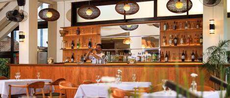 A restaurant interior with wooden tables, chairs, and a bar area with shelves of bottles.
