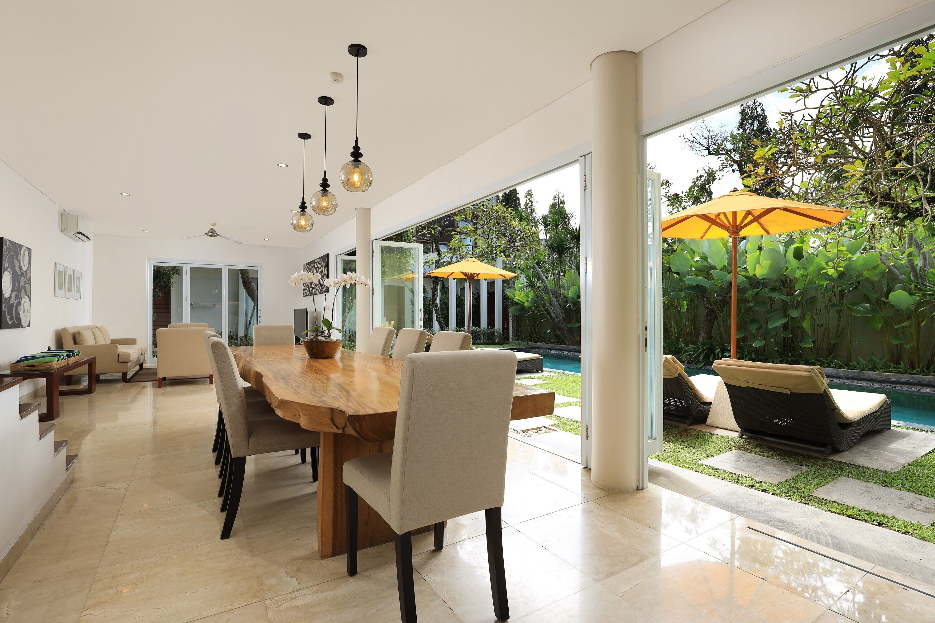 Un comedor moderno con una gran mesa de madera, sillas cómodas y vistas a una piscina y jardín.