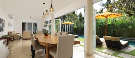 Un comedor moderno con una gran mesa de madera, sillas cómodas y vistas a una piscina y jardín.