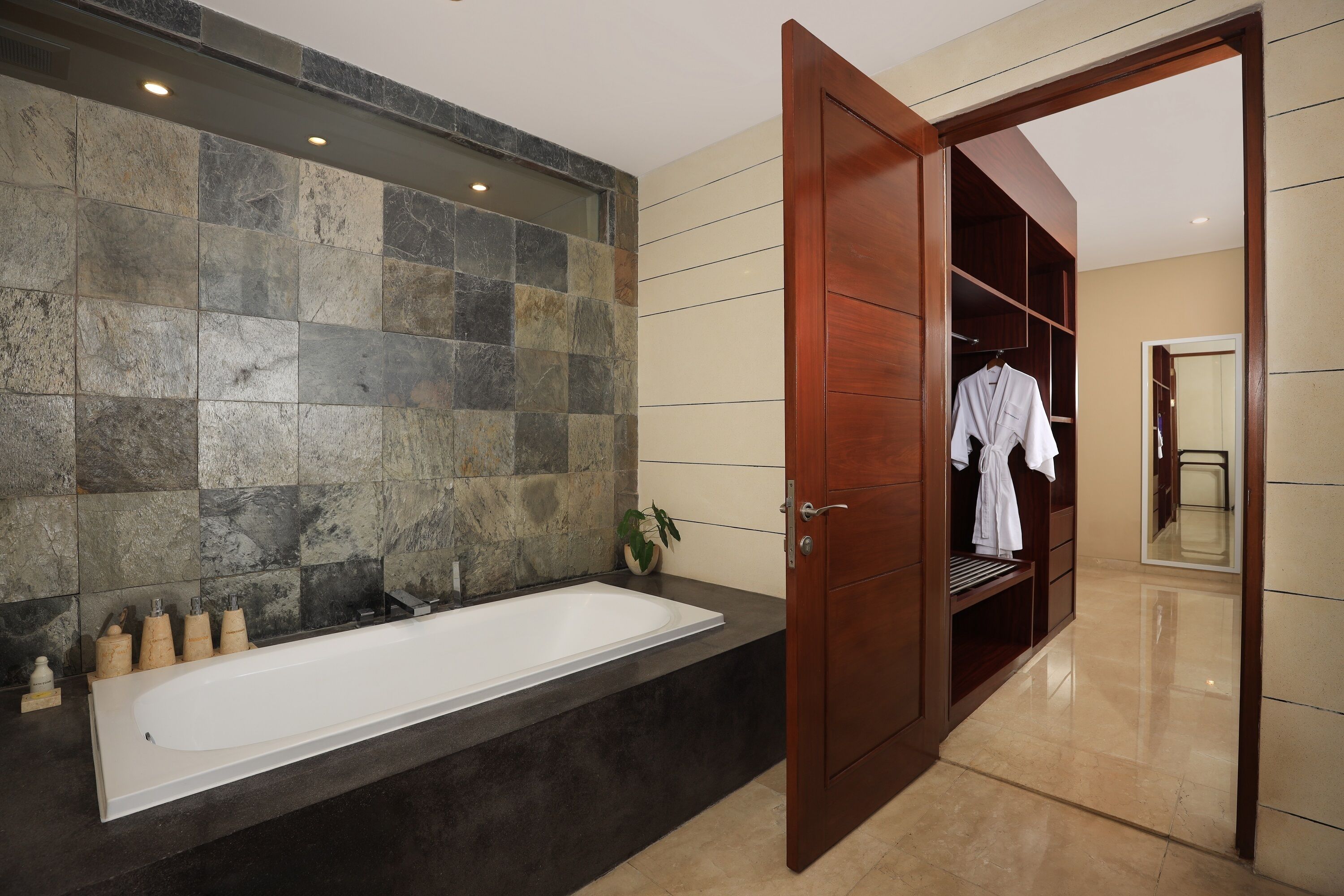 A modern bathroom with a large bathtub, a wooden vanity, and a walk-in closet with a mirror.