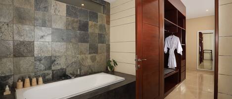 Un baño moderno con una bañera grande, un tocador de madera y un vestidor con espejo.