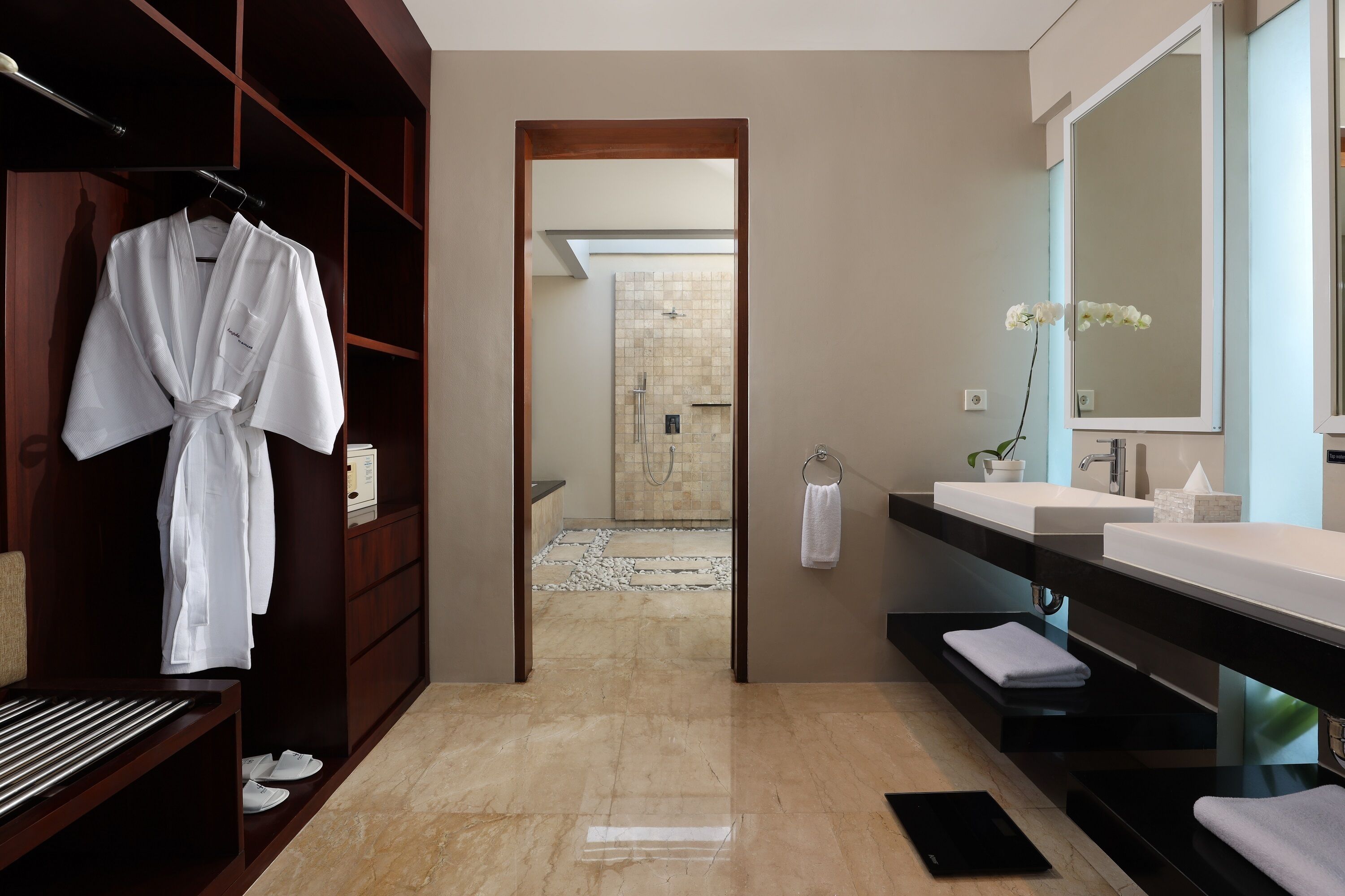 Un bagno moderno con doccia a filo pavimento, un mobile vanitario con un ampio specchio e un accappatoio appeso a un appendiabiti.