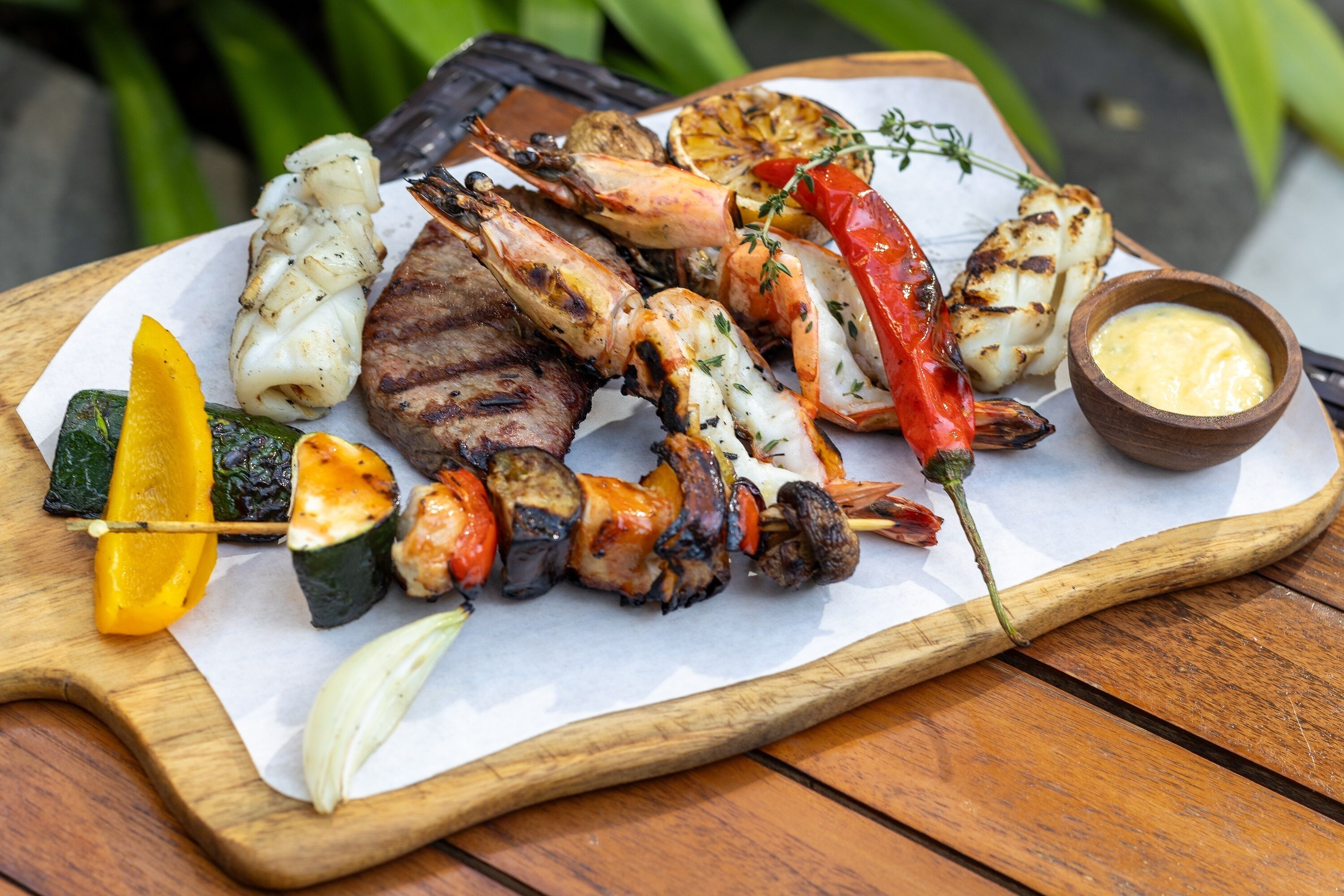 A variety of grilled seafood and vegetables on a wooden board.
