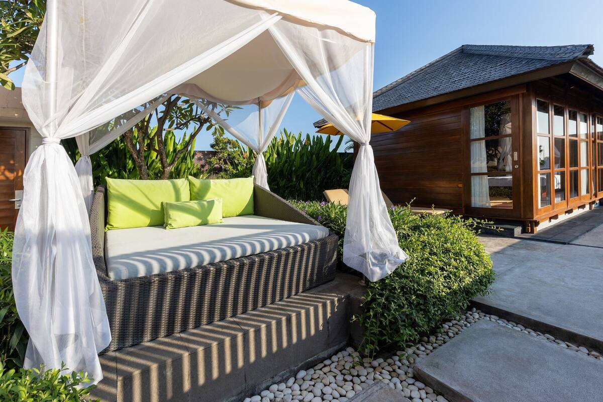 A bed with a canopy, green cushions, and a view of a wooden building.