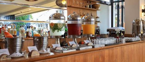 Zona de bar con varios dispensadores de bebidas, una barra de madera y estantes con botellas y vasos.