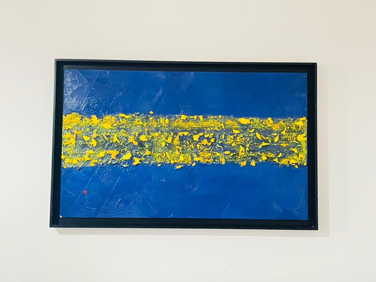 En inramad abstrakt målning med blå och gula färger.