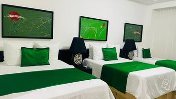 Quarto de hotel com três camas, cada uma com colcha verde e roupa de cama branca. Há três quadros abstratos nas paredes, e uma luminária preta com design em espiral no criado-mudo.