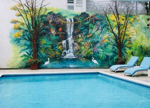 A swimming pool with a mural of a waterfall and tropical foliage. There are lounge chairs and potted plants. - Hotel Galerias Hn (San Pedro Sula)