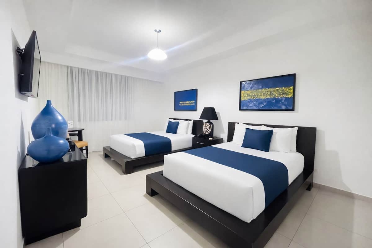 Ein Hotelzimmer mit zwei Betten, einem Flachbildfernseher, einem Schreibtisch und einem Sessel.