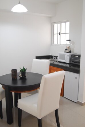 Compact kitchen with dining area, featuring a microwave, refrigerator, sink, and dining table with chairs.