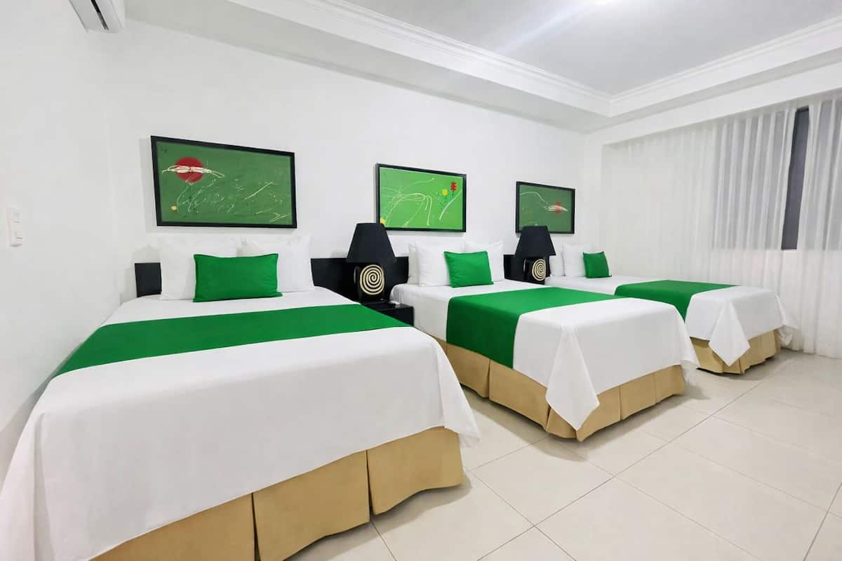 Ein Hotelzimmer mit drei Betten, jedes mit einer grün-weißen Tagesdecke, weißen Kissen und einem Nachttisch mit Lampe.