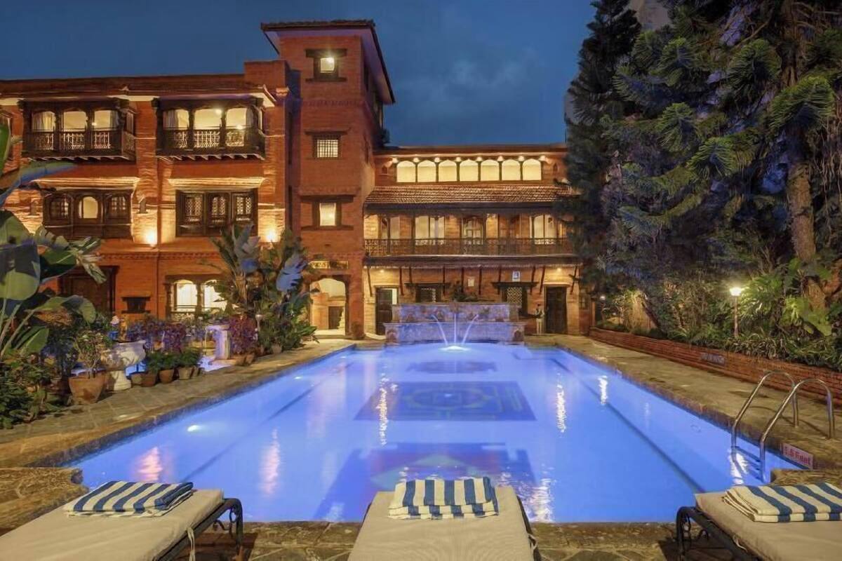Una piscina con sillas de descanso, una fuente de agua y un edificio con varios balcones y ventanas.