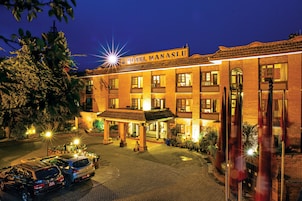 A hotel with a sign reading "HOTEL MANASLJU," featuring a traditional architectural style with multiple balconies and a paved courtyard.