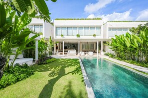 A modern house with a swimming pool, covered patio, and lush greenery.