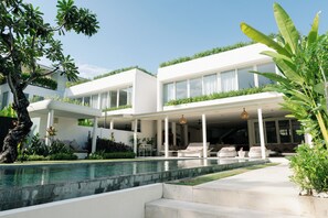 A modern house with a pool, covered patio, and lush greenery.