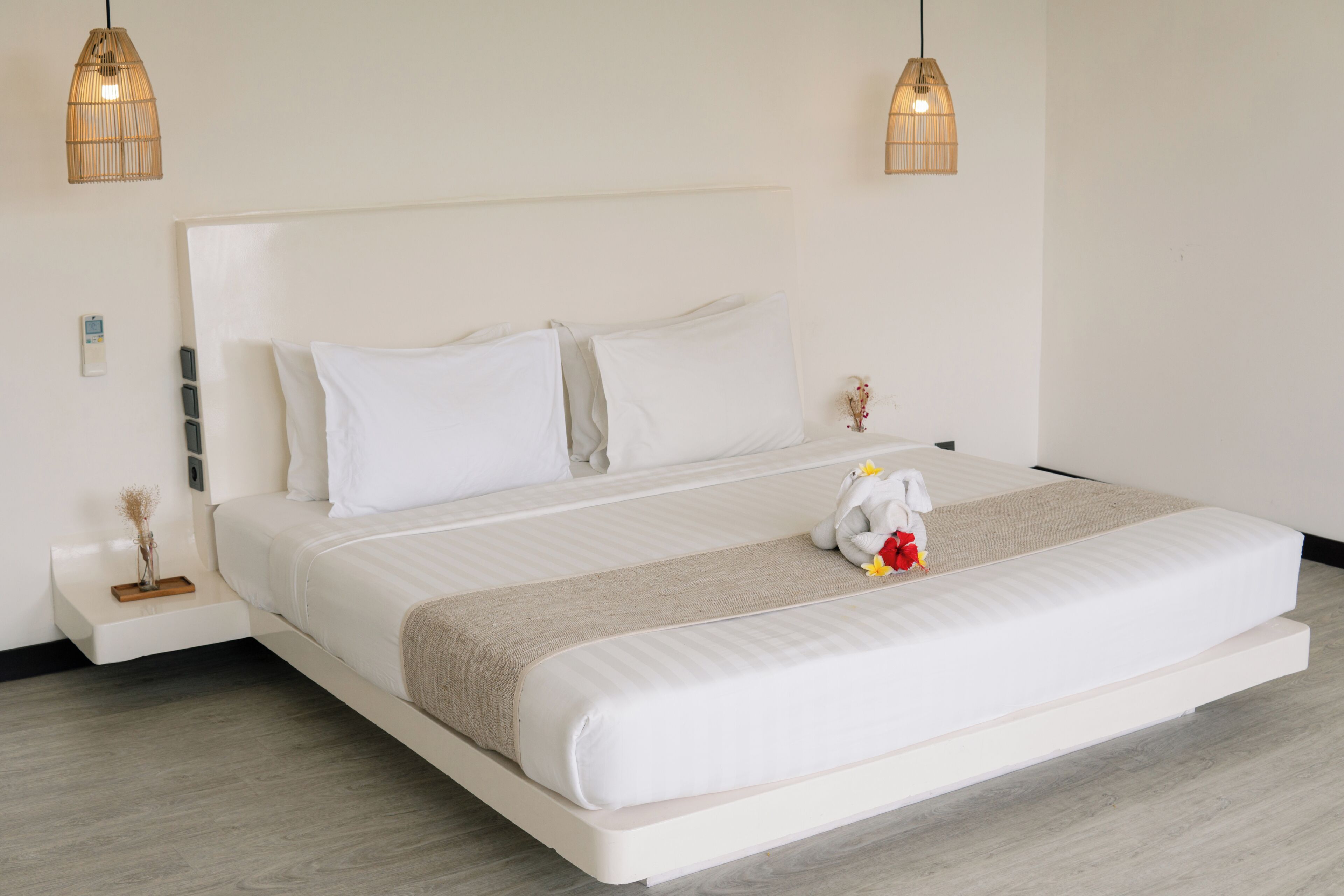 Una habitación de hotel moderna con una cama grande, dos lámparas de noche, una mesita de noche y un pequeño jarrón con flores secas.