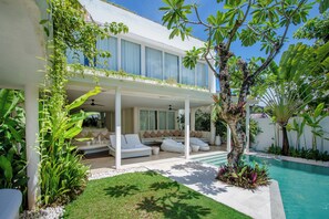 A modern house with a pool, outdoor seating, and lush greenery.