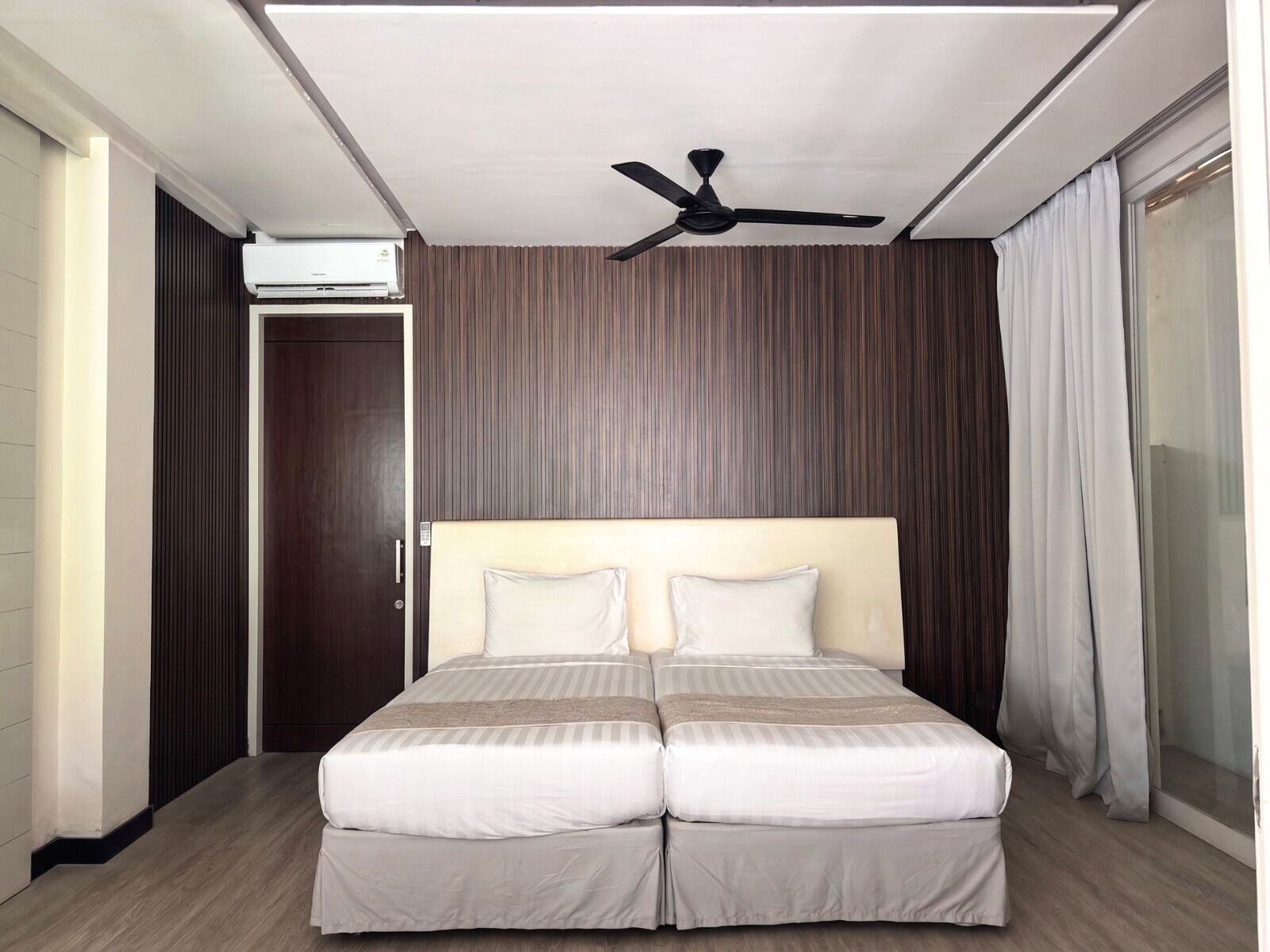 Een tweepersoonsbed met hoofdeinde, een plafondventilator, een airconditioner en een schuifdeur.