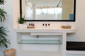 A bathroom with a white sink, a mirror, and a glass shelf below the sink.