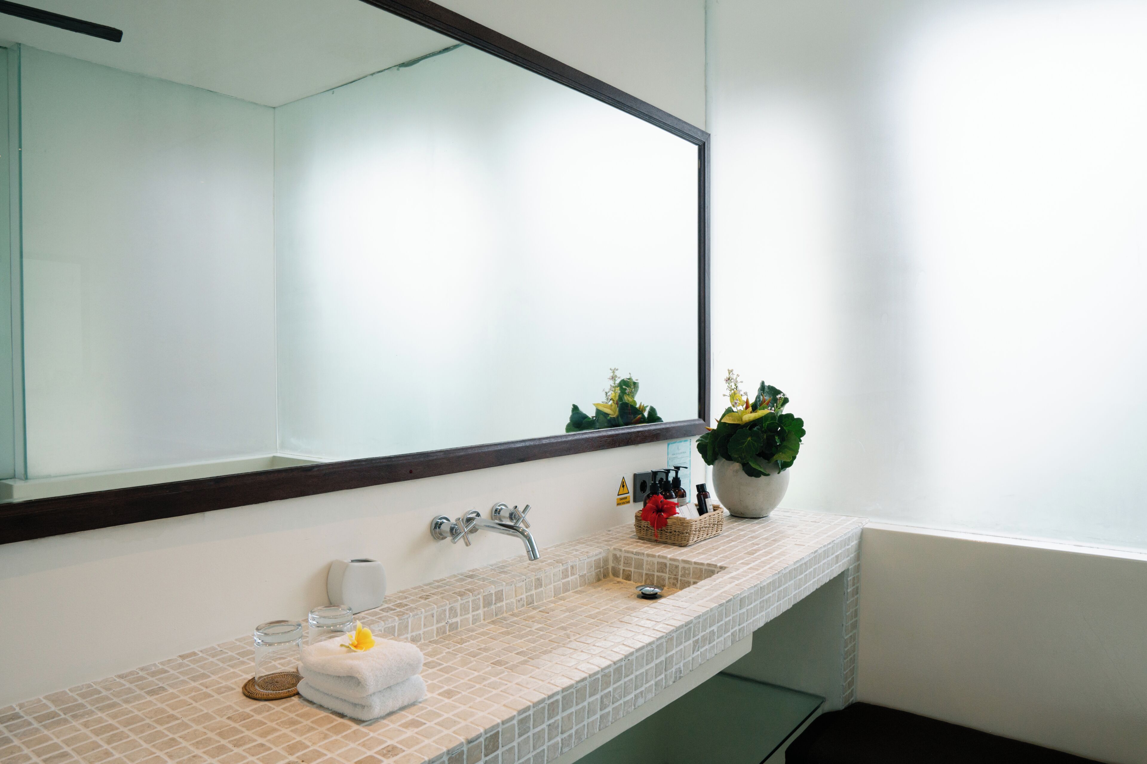 Une salle de bain avec un grand miroir, un lavabo, une serviette, une petite plante et un flacon de lotion.