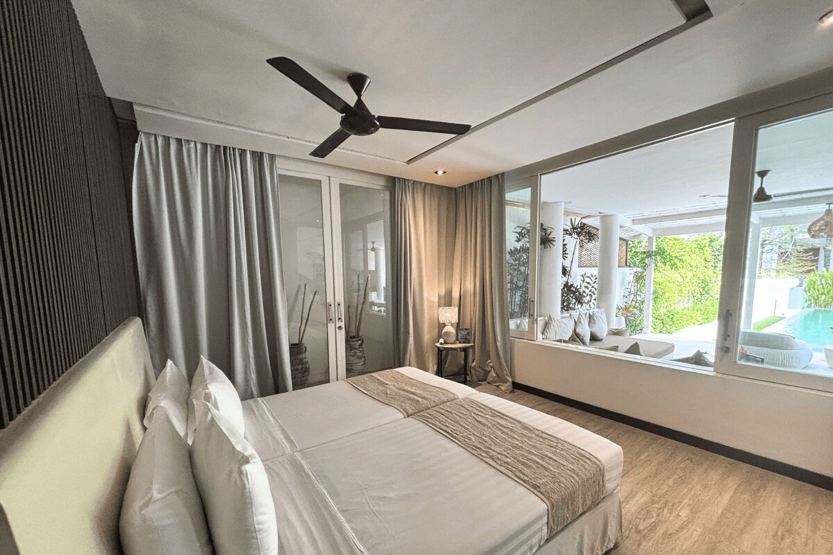 A bedroom with a bed, curtains, a ceiling fan, and a view of the outdoors.