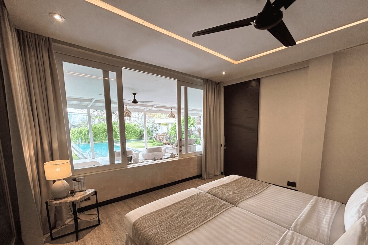 A hotel room with a large bed, a ceiling fan, a view of a swimming pool, and a window with curtains.