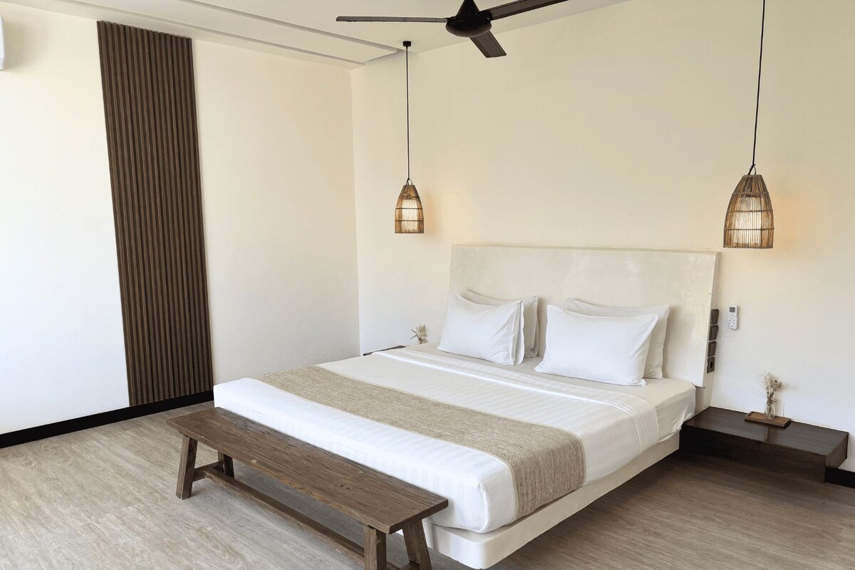 A bedroom with a bed, a bench, a ceiling fan, and two wall-mounted lamps.