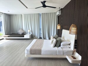 A modern bedroom with a large bed, a bedside table with a lamp, a ceiling fan, and a wall-mounted air conditioner. -  Eden The Residence at The Sea Seminyak (Seminyak)