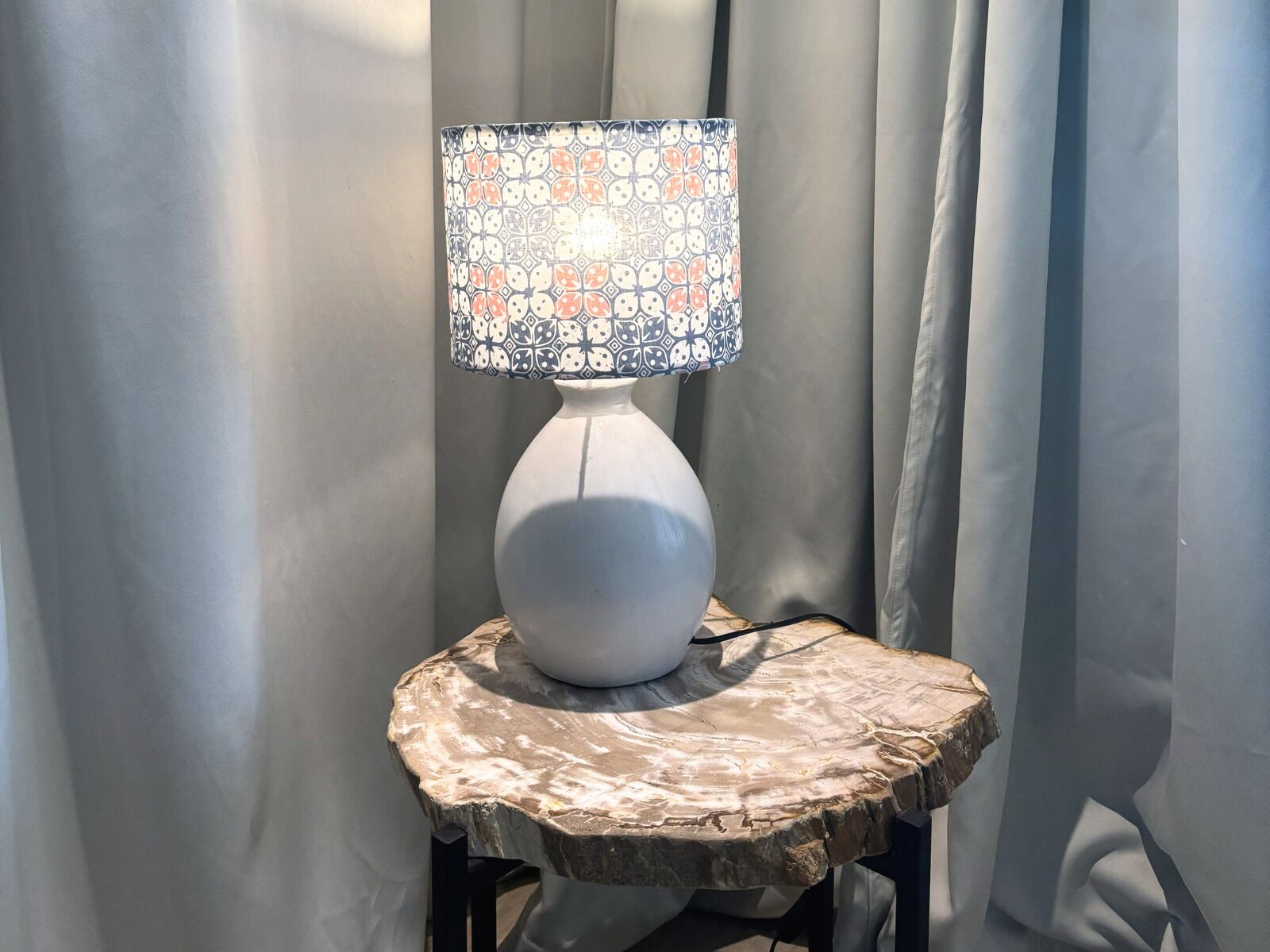 A white table lamp with a patterned lampshade on a rustic wooden table.