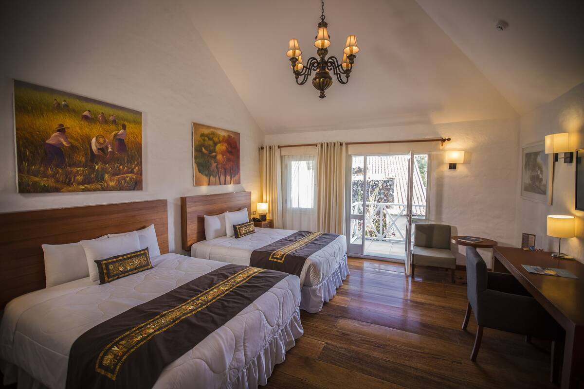 A hotel room with two beds, a chandelier, a desk, and a balcony with a view.