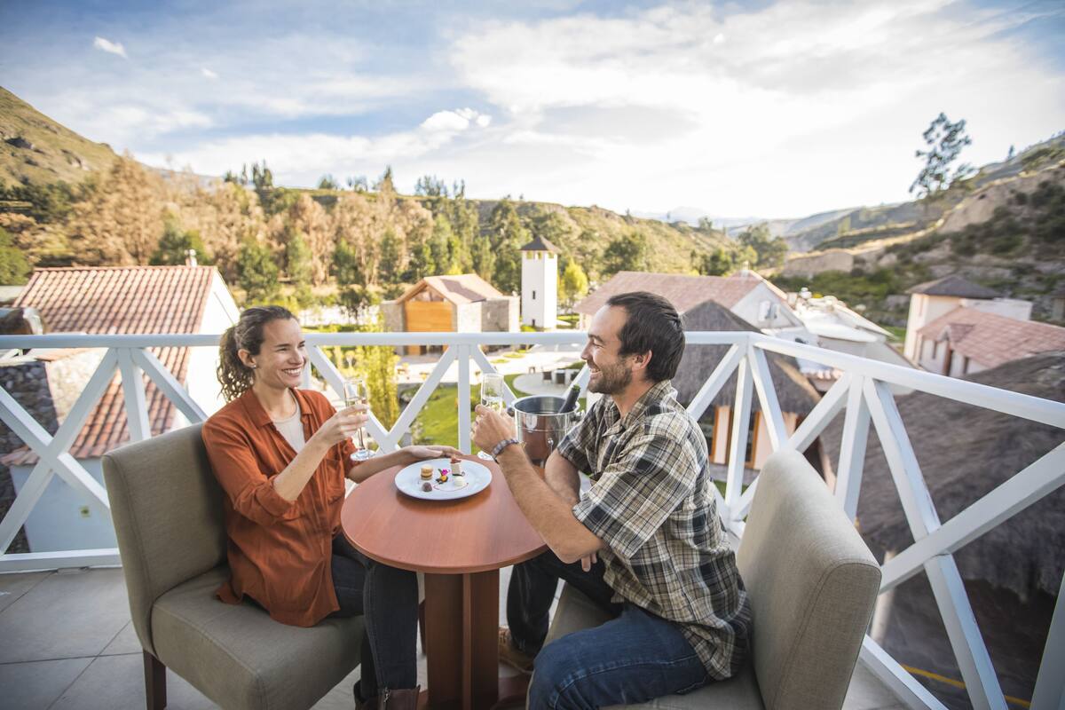 Two people seated at a table with a plate of food, overlooking a scenic village with houses and a church.