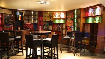 A cozy bar area with a round table and multiple bar stools, surrounded by shelves with various bottles and decorative items.