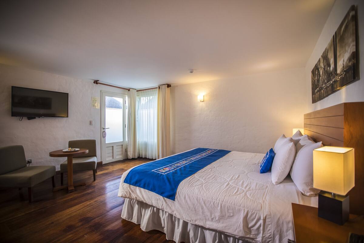 A hotel room with a bed, a desk, a chair, a TV, and a window with curtains.