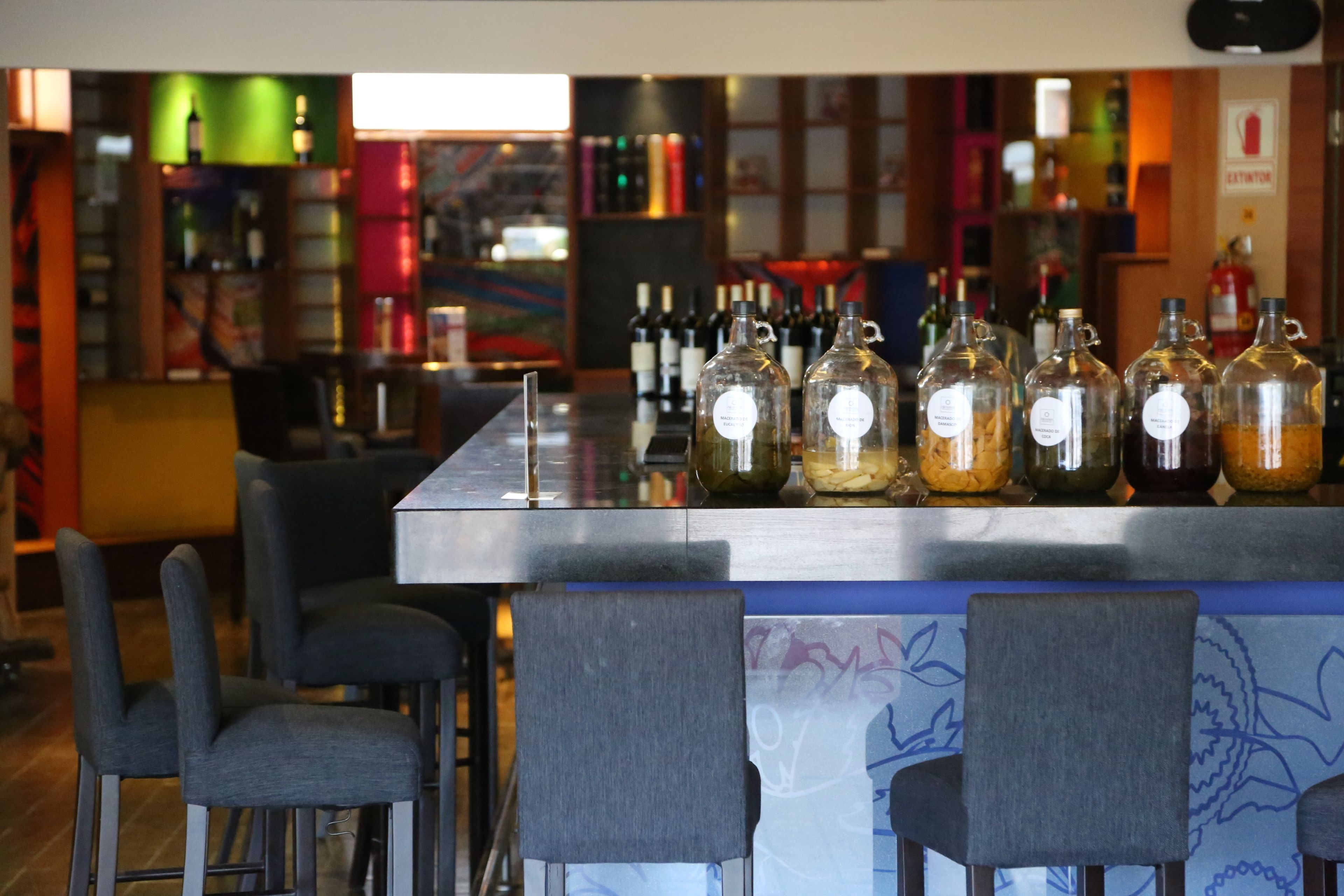 A bar area with a counter displaying various bottles, bar stools, and a colorful mural in the background.