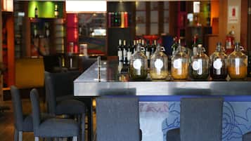 A bar area with a counter displaying various bottles, bar stools, and a colorful mural in the background.