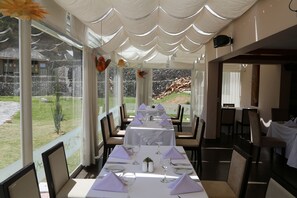 A restaurant with a long table set for a meal, large windows, and a view of the outdoors.