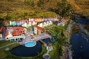 An aerial view of a resort with colorful buildings, a swimming pool, and a river.