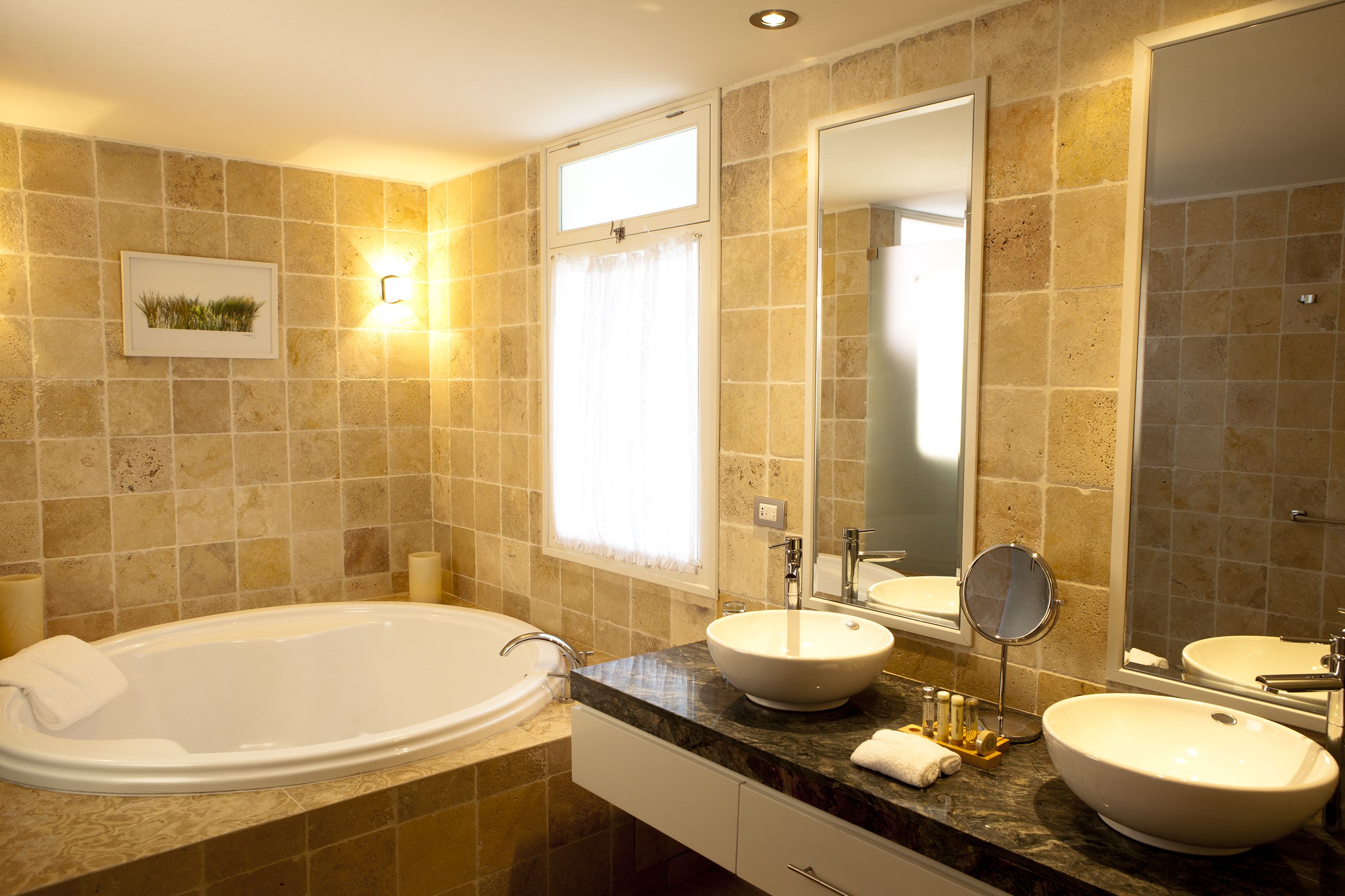 A bathroom with a bathtub, two sinks, a large mirror, and a framed picture on the wall.