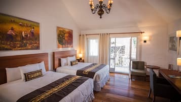 A hotel room with two beds, a chandelier, a painting, a desk, and a view through a glass door.