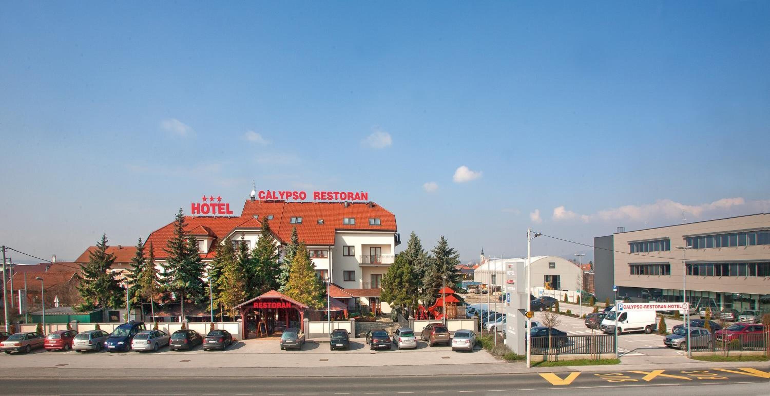 Un hotel con techo rojo y un restaurante en la planta baja. Varias coches estacionados en la entrada.