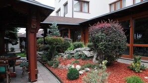 A courtyard with a covered seating area, a stone wall, and various shrubs and plants.
